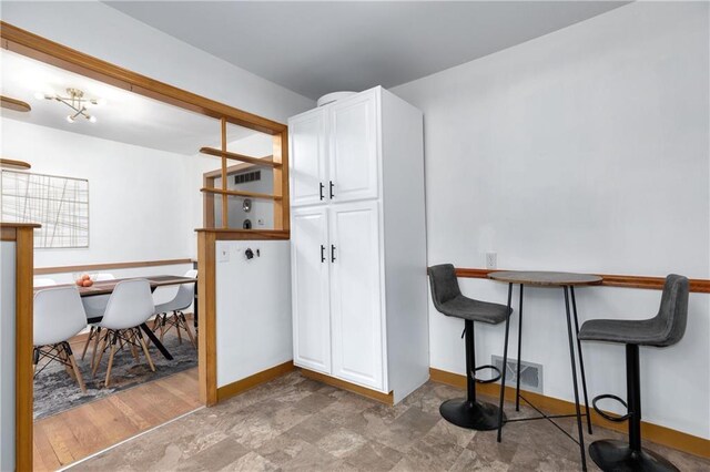 kitchen featuring a breakfast bar area, white cabinetry, visible vents, and baseboards