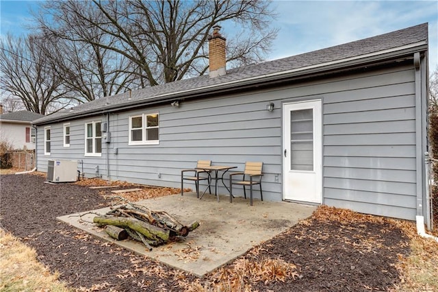 back of house with a patio, a chimney, and roof with shingles