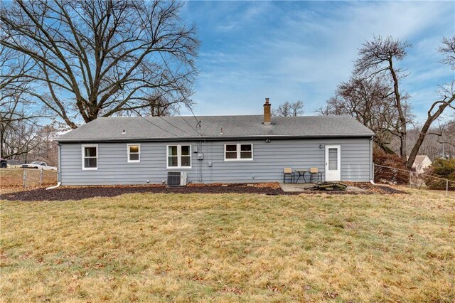 rear view of house with central AC unit, a chimney, fence, and a yard