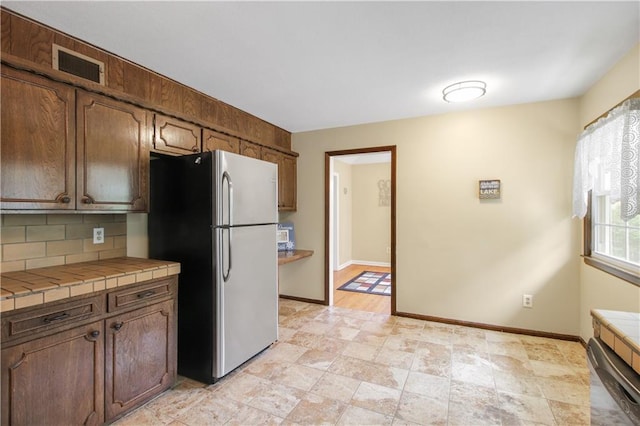 kitchen with tasteful backsplash, tile counters, and stainless steel fridge