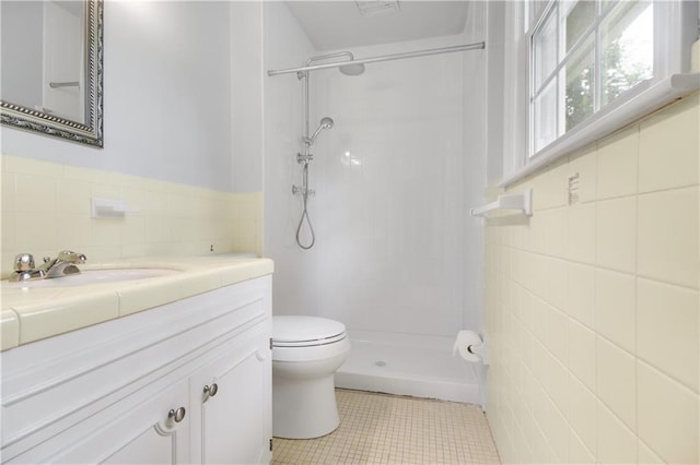 bathroom with tiled shower, toilet, tile walls, vanity, and tile patterned flooring