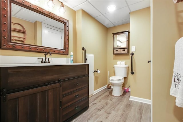 bathroom featuring a drop ceiling, vanity, wood-type flooring, and toilet