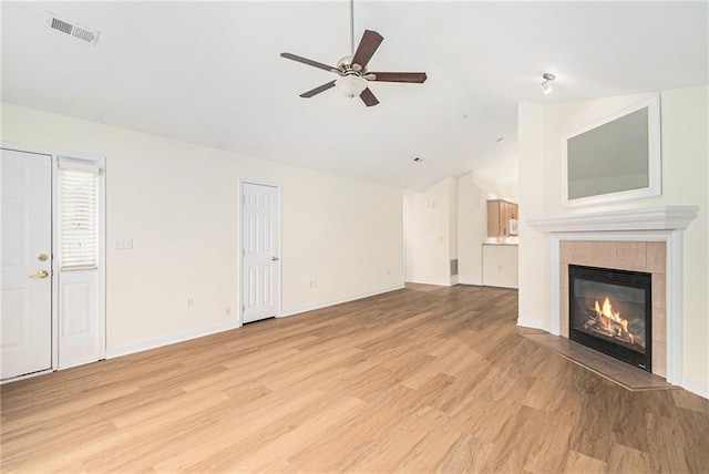 unfurnished living room with a tiled fireplace, lofted ceiling, ceiling fan, and light wood-type flooring