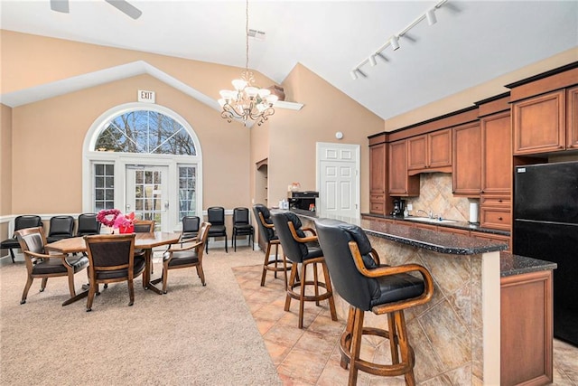 kitchen with black refrigerator, backsplash, dark stone countertops, a kitchen bar, and decorative light fixtures