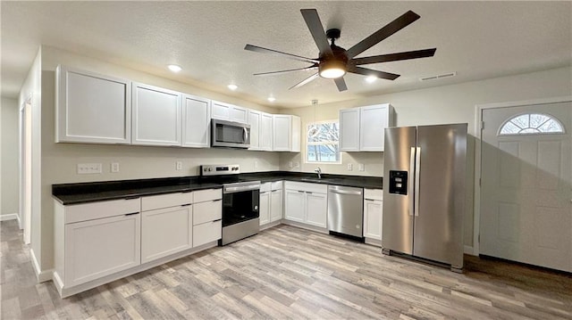 kitchen with a textured ceiling, ceiling fan, stainless steel appliances, light hardwood / wood-style floors, and white cabinets