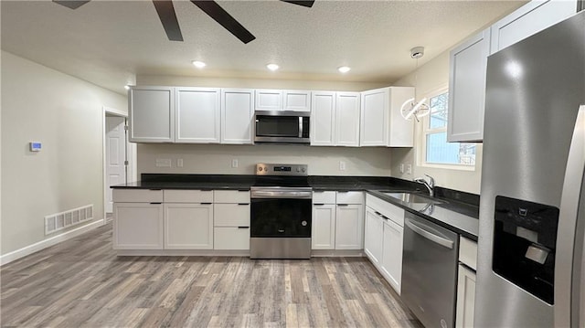 kitchen with appliances with stainless steel finishes, decorative light fixtures, sink, white cabinets, and light hardwood / wood-style floors