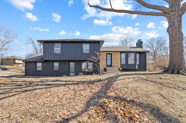 tri-level home featuring board and batten siding, brick siding, and a chimney