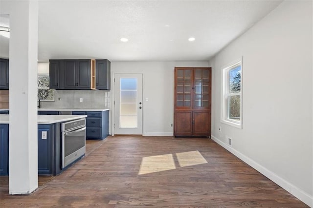 7901 Hedges Ave, Raytown, MO 64138 - kitchen with backsplash, wood finished floors, light countertops, stainless steel oven, and baseboards