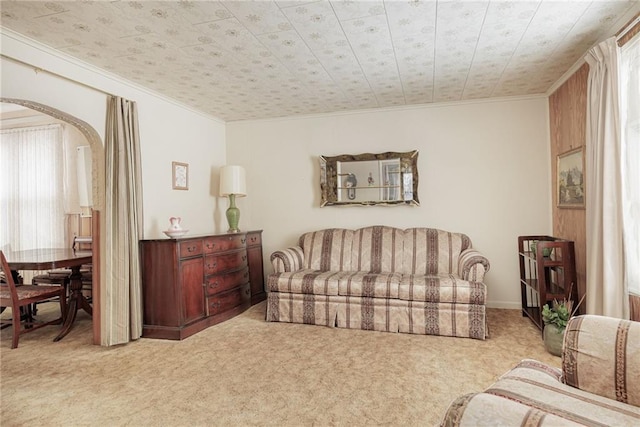 living area featuring arched walkways, crown molding, and light colored carpet