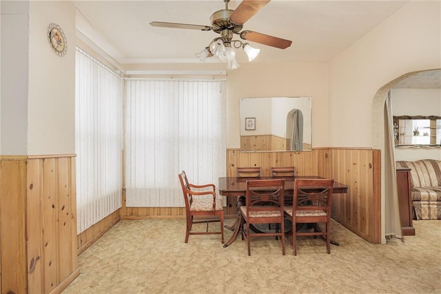 dining room featuring a wainscoted wall, arched walkways, and light colored carpet