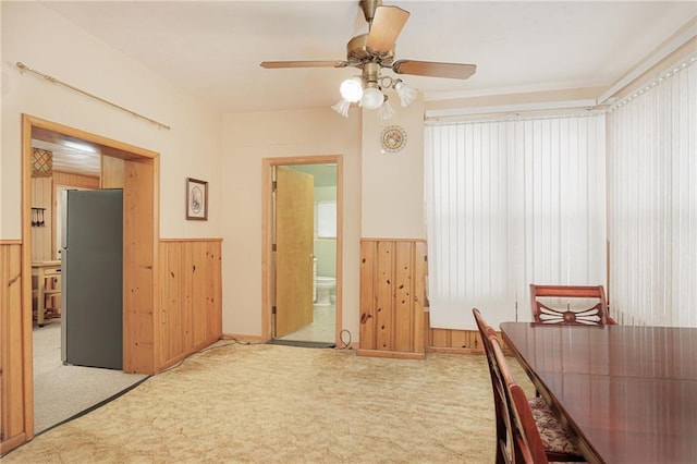 unfurnished dining area featuring carpet floors, wainscoting, wooden walls, and a ceiling fan