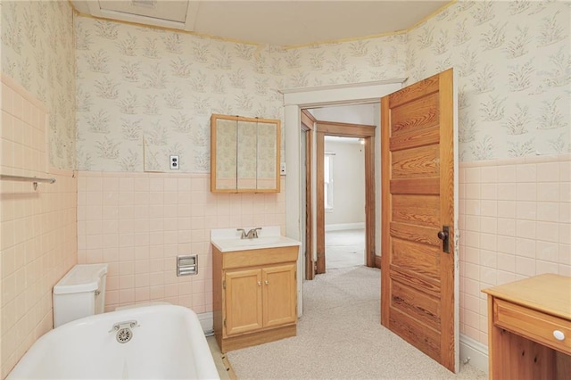 bathroom with tile walls, toilet, wainscoting, vanity, and wallpapered walls