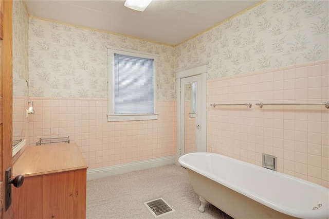 bathroom featuring a wainscoted wall, a freestanding bath, visible vents, and wallpapered walls