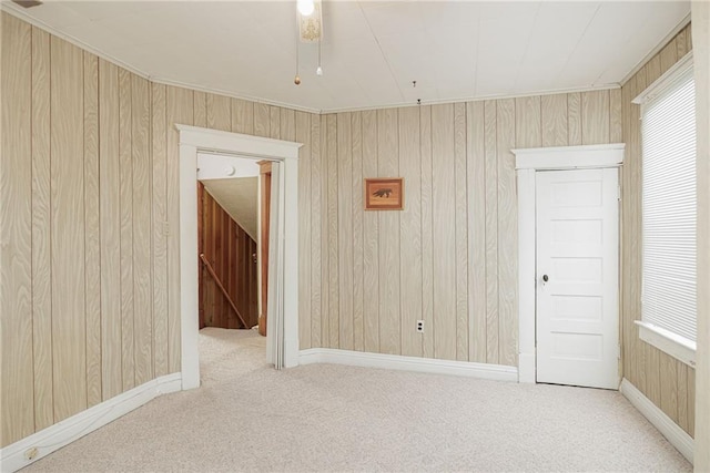 carpeted empty room with plenty of natural light, wooden walls, and baseboards