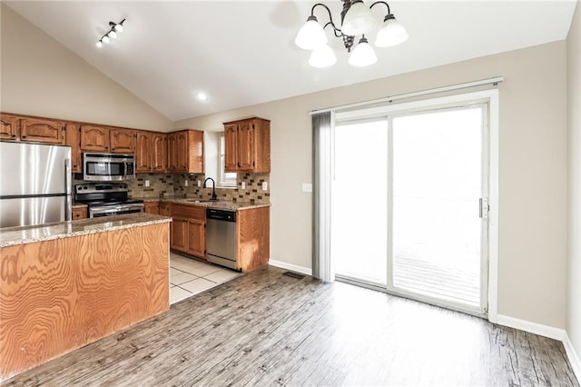 kitchen with lofted ceiling, sink, stainless steel appliances, light stone countertops, and decorative backsplash