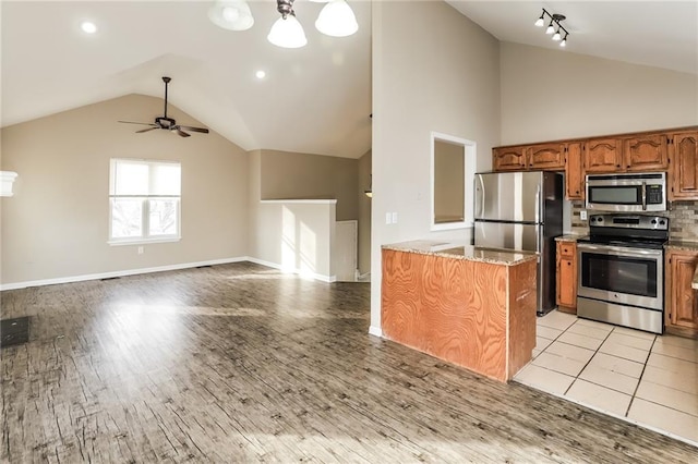 kitchen with stainless steel appliances, vaulted ceiling, ceiling fan, and light hardwood / wood-style flooring