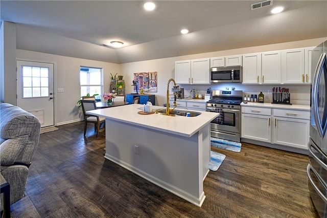 kitchen with appliances with stainless steel finishes, white cabinetry, lofted ceiling, sink, and a kitchen island with sink