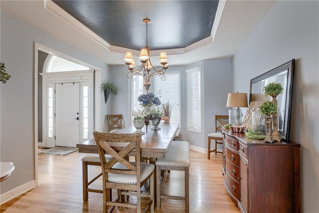 dining space with light wood-style floors, baseboards, a tray ceiling, and a chandelier