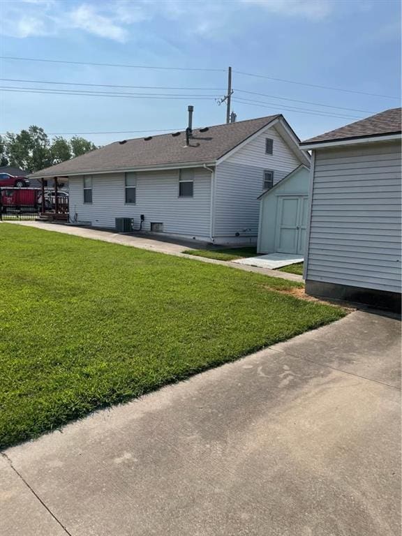 back of house featuring a shed, a patio area, a lawn, cooling unit, and an outbuilding