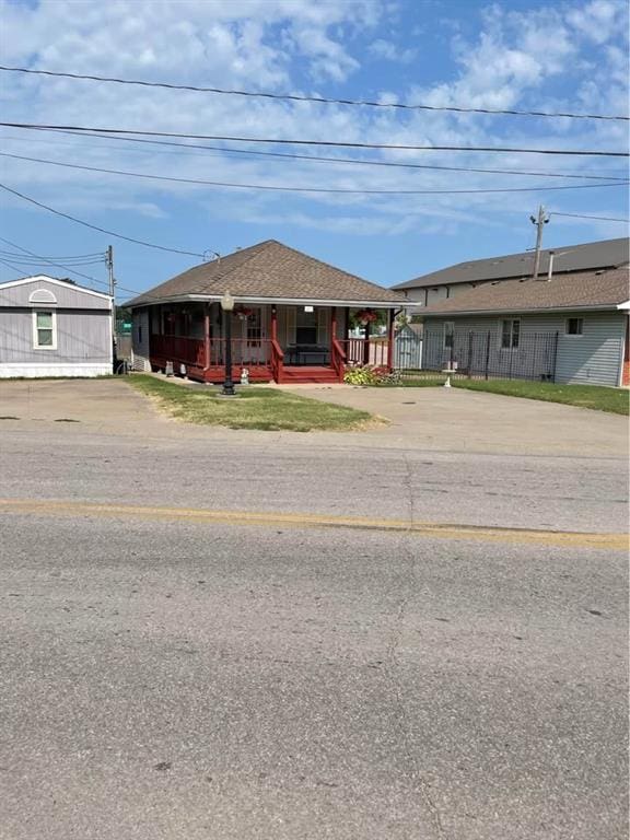 view of front of home featuring roof with shingles, covered porch, and fence private yard