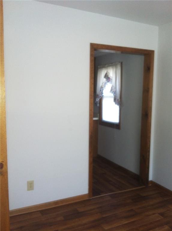 corridor featuring dark wood-type flooring and baseboards