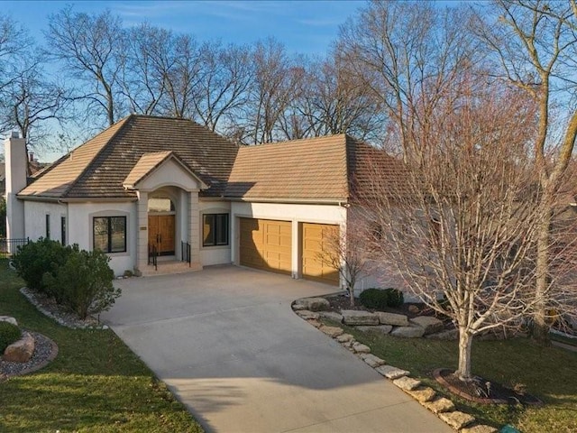 view of front of house with stucco siding, an attached garage, a chimney, and driveway