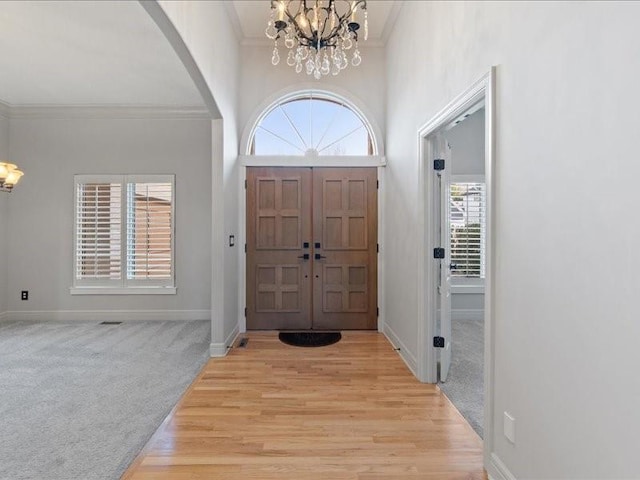 entryway featuring crown molding, baseboards, light colored carpet, arched walkways, and a notable chandelier