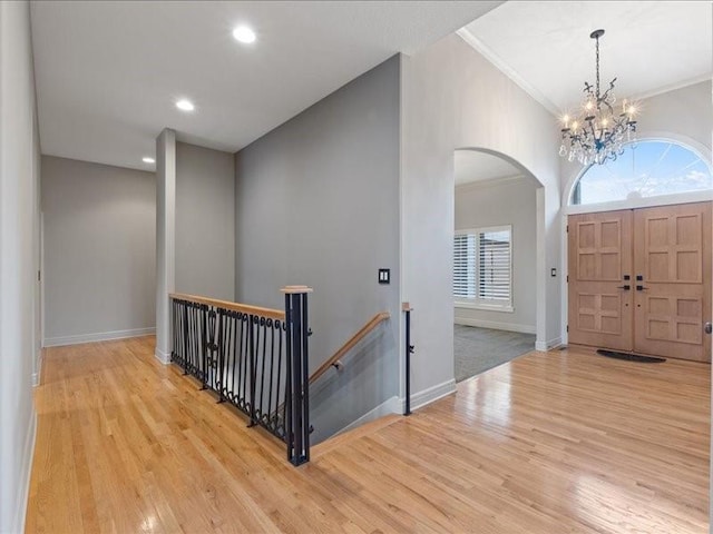 foyer entrance with crown molding, arched walkways, light wood finished floors, and a chandelier