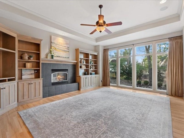 unfurnished living room featuring a tray ceiling, plenty of natural light, light wood-style flooring, and a tile fireplace