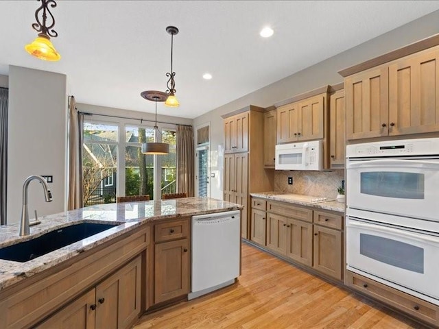 kitchen featuring light wood finished floors, tasteful backsplash, decorative light fixtures, white appliances, and a sink