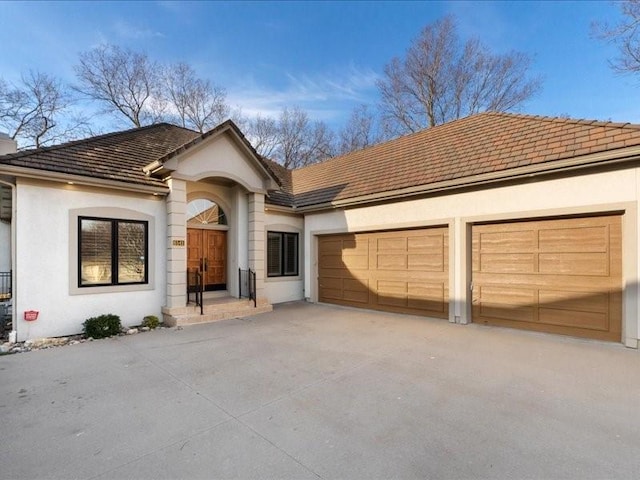 single story home featuring stucco siding, concrete driveway, an attached garage, and a tile roof