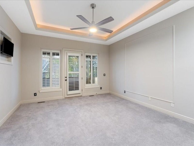 spare room featuring light carpet, baseboards, a raised ceiling, and a ceiling fan