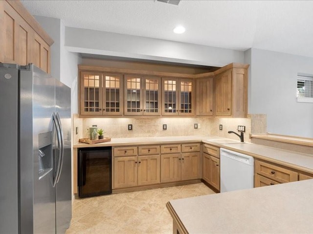 kitchen with beverage cooler, white dishwasher, glass insert cabinets, stainless steel fridge, and backsplash