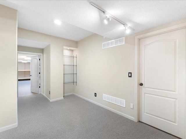 carpeted empty room featuring track lighting, baseboards, and visible vents