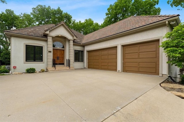 ranch-style home featuring driveway, a tiled roof, an attached garage, and stucco siding