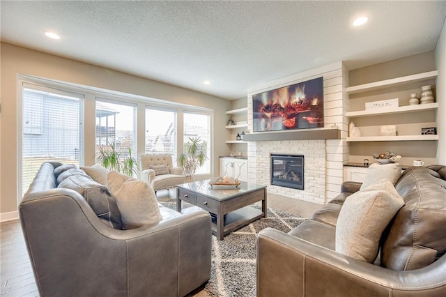 living room with a brick fireplace, hardwood / wood-style floors, a textured ceiling, and built in shelves