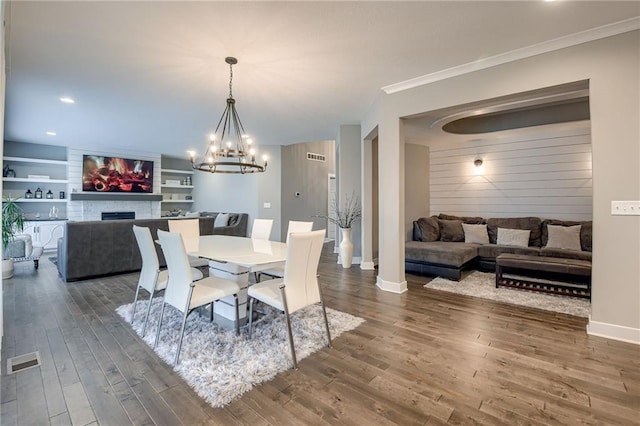 dining space featuring built in shelves, ornamental molding, dark hardwood / wood-style flooring, and a chandelier