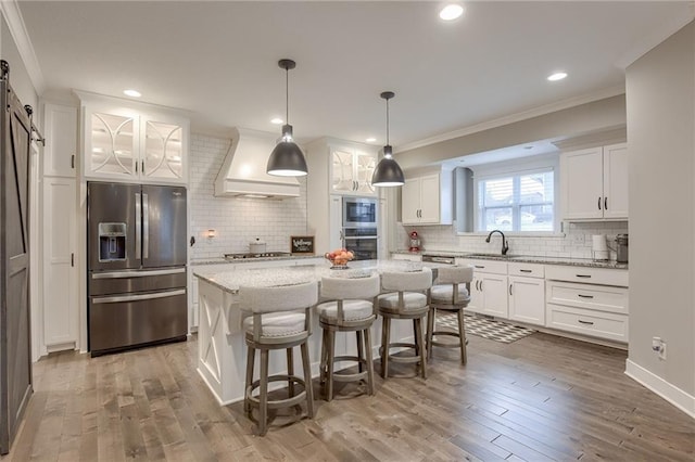 kitchen with custom exhaust hood, white cabinetry, a kitchen island, stainless steel appliances, and a barn door