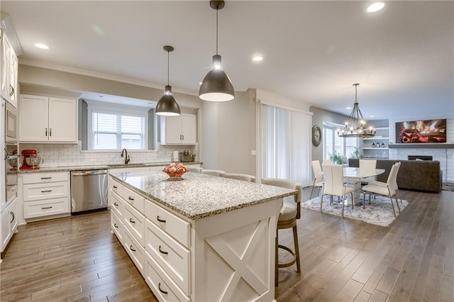 kitchen featuring a kitchen island, decorative light fixtures, sink, white cabinets, and stainless steel dishwasher