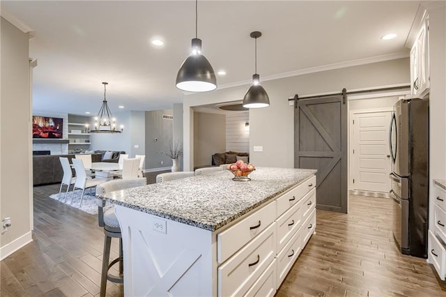 kitchen with a kitchen island, a breakfast bar, white cabinetry, stainless steel fridge, and a barn door