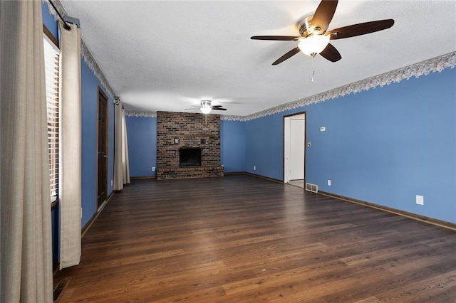 unfurnished living room featuring ceiling fan, dark hardwood / wood-style flooring, a brick fireplace, and a textured ceiling