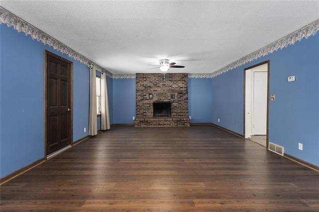 unfurnished living room featuring dark wood-type flooring, ceiling fan, a brick fireplace, and a textured ceiling