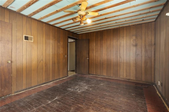 spare room featuring dark wood-type flooring, ceiling fan, and wood walls