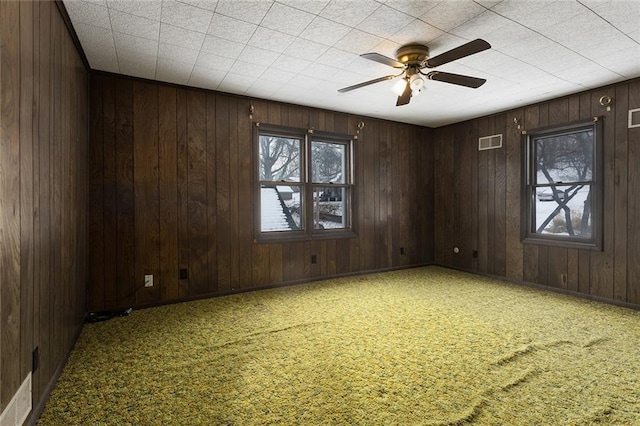 unfurnished room featuring carpet, a wealth of natural light, and wooden walls