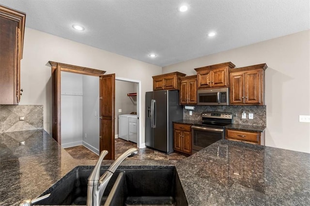 kitchen featuring washer and clothes dryer, a sink, tasteful backsplash, appliances with stainless steel finishes, and brown cabinetry