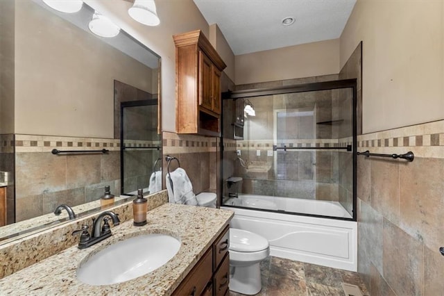 full bathroom with vanity, a wainscoted wall, bath / shower combo with glass door, tile walls, and toilet