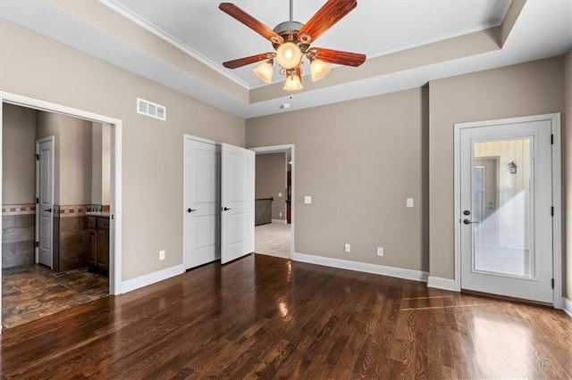 unfurnished bedroom featuring visible vents, baseboards, a tray ceiling, and wood finished floors