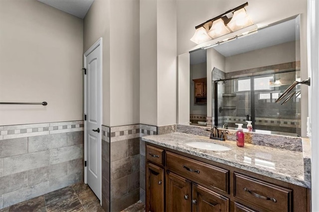 bathroom with wainscoting, tile walls, a stall shower, and vanity