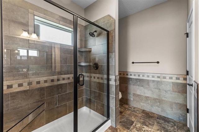 full bathroom with a shower stall, toilet, wainscoting, stone finish floor, and tile walls