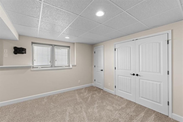 unfurnished bedroom with a closet, a drop ceiling, baseboards, and carpet